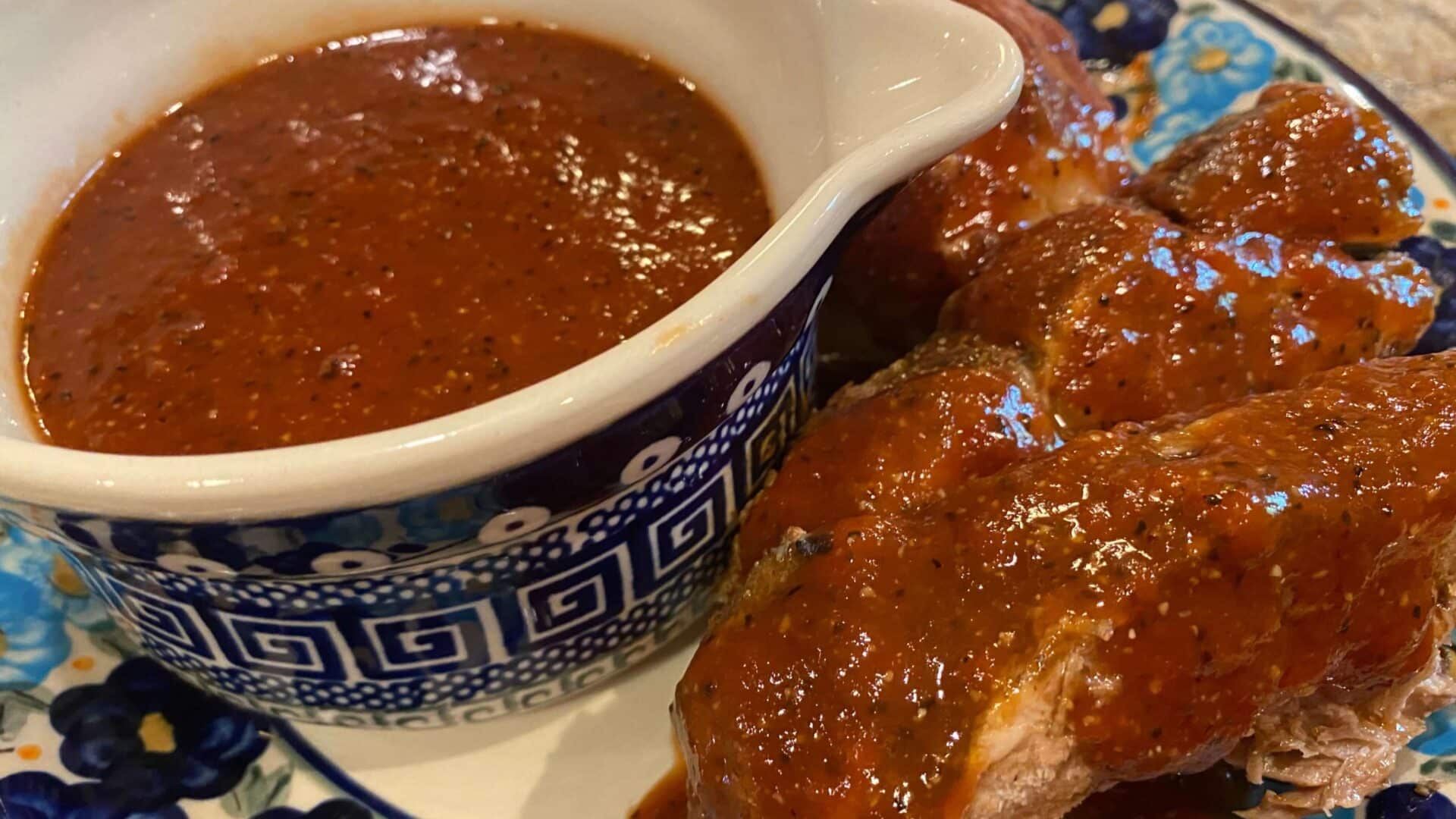 red sauce with specs of pepper and other spices on ribs, chicken and in a blue and white bowl