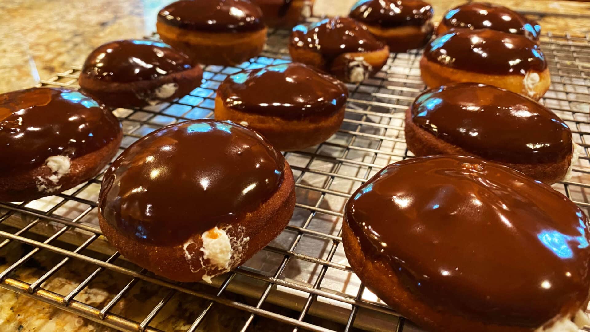 Golden round doughnuts with a chocolate glistening glaze on top and white cream oozing from inside