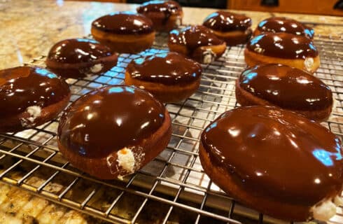 Golden round doughnuts with a chocolate glistening glaze on top and white cream oozing from inside