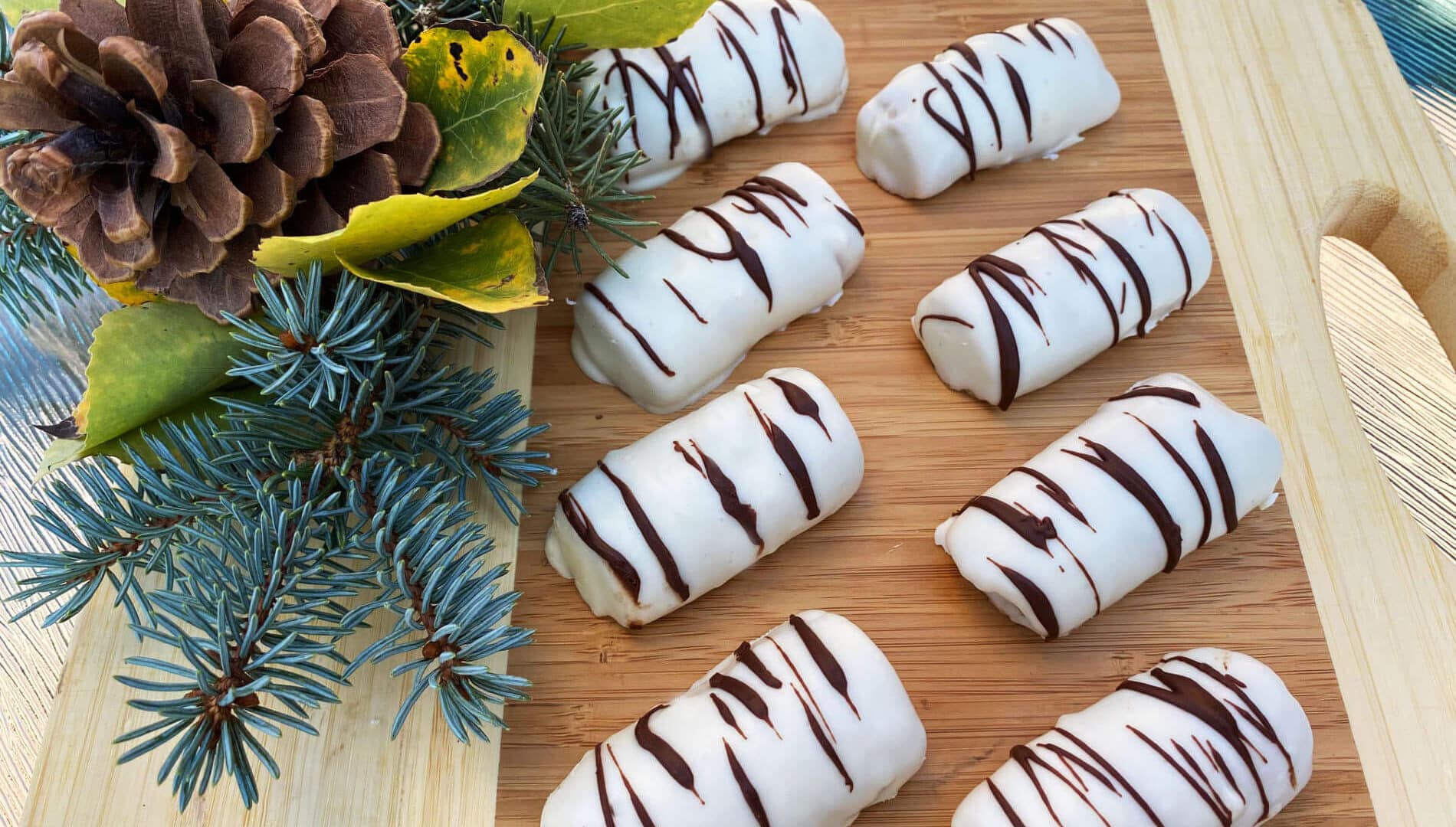 White chocolate coated cookies with dark chocolate stripes, looking like birch logs, with green pine branches, yellow aspen leaves, and a brown pine cone