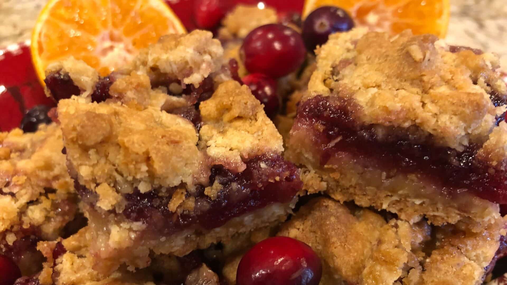 Square bar cookies with golden crumble crust and red filling adorned with cranberries and oranges