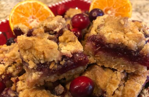 Square bar cookies with golden crumble crust and red filling adorned with cranberries and oranges