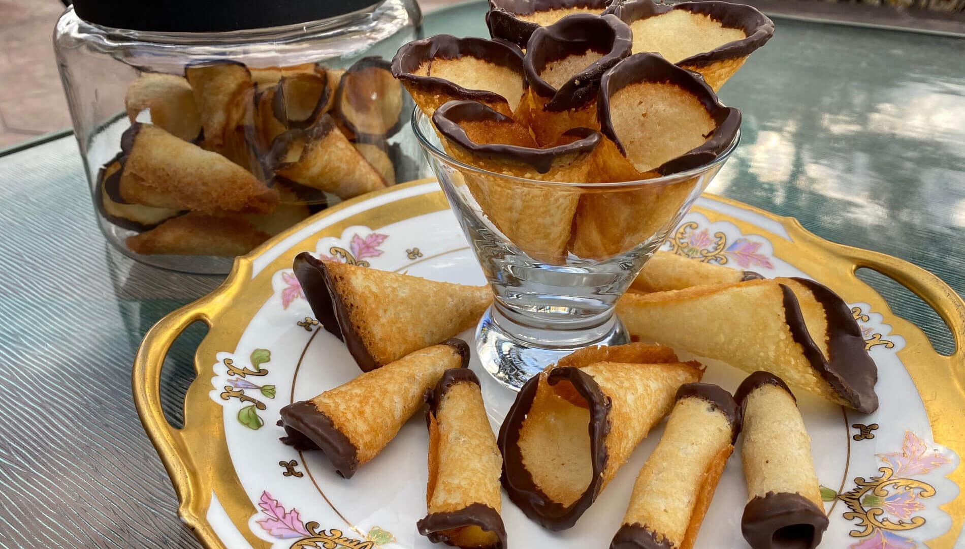 Cone shaped golden cookies in a martini glass and on a plate with the edges dipped in chocolate