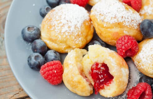 round pancake balls filled with red jam, dusted with powdered sugar and tossed with red and blue beries