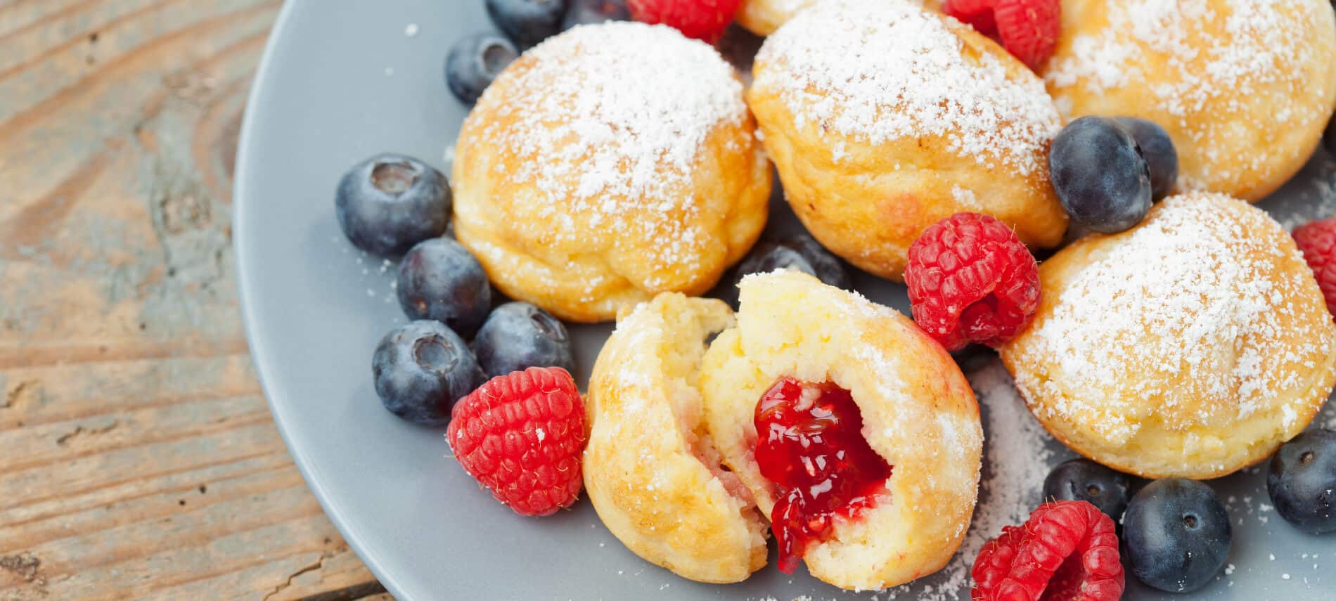 round pancake balls filled with red jam, dusted with powdered sugar and tossed with red and blue beries