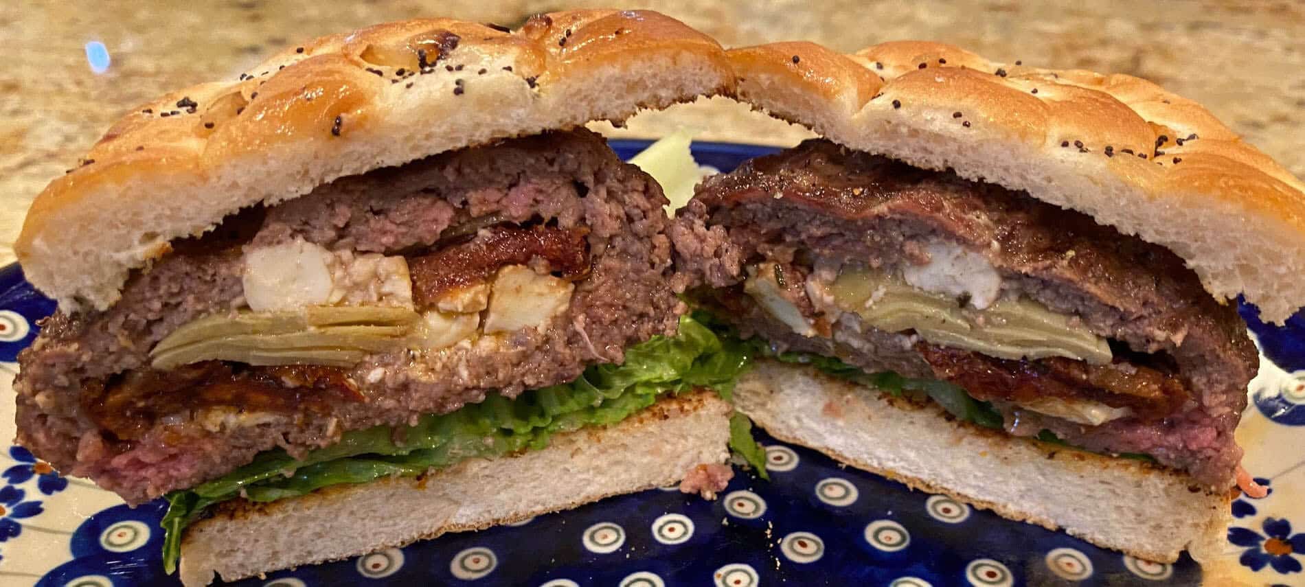 ground beef burger stuffed with feta cheese, artichoke hearts and sundried tomatoes on an onion and poppyseed bun