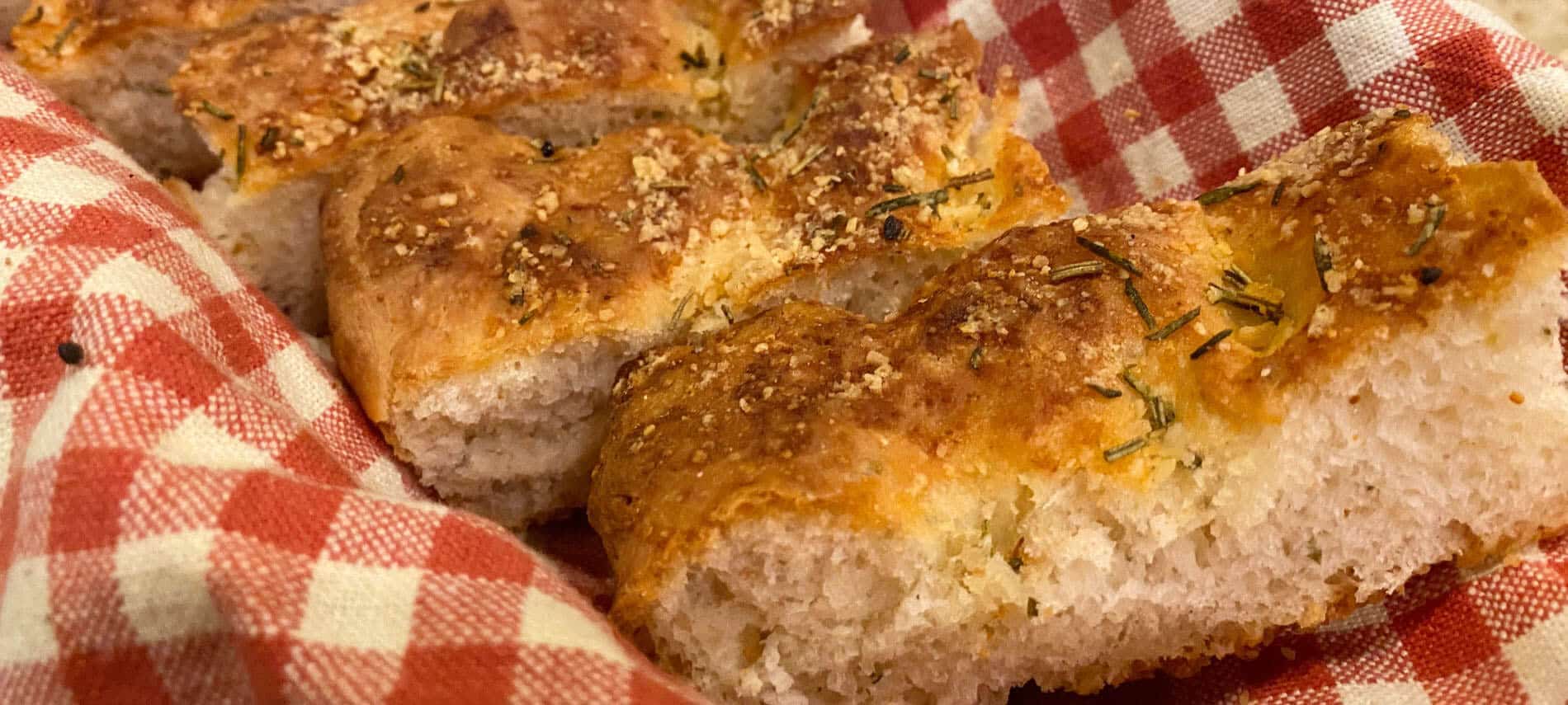 Slices of focaccia bread with rosemary and sea salt on a red and white checkered cloth