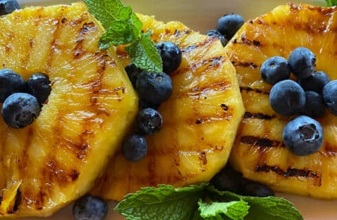 Grilled Pineapple Slices with blueberries and mint leaves on a white plate