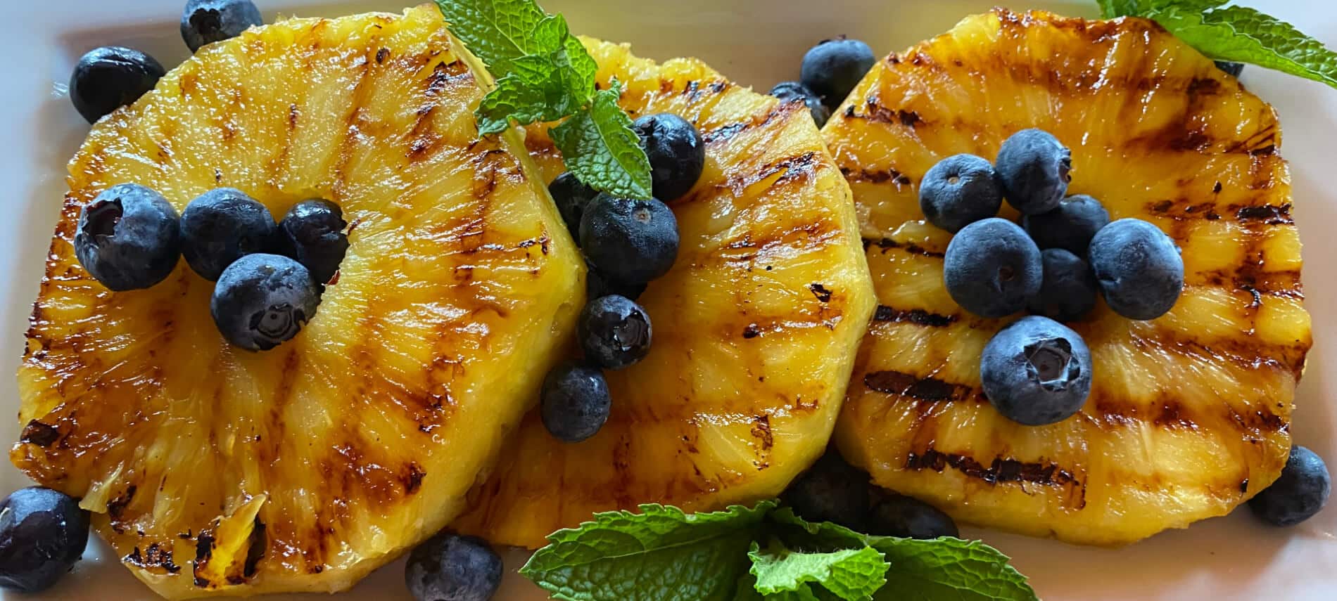 Grilled Pineapple Slices with blueberries and mint leaves on a white plate