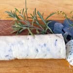 Log of white butter with flecks of herbs in the butter with fresh rosemary, sage leaves, and thyme
