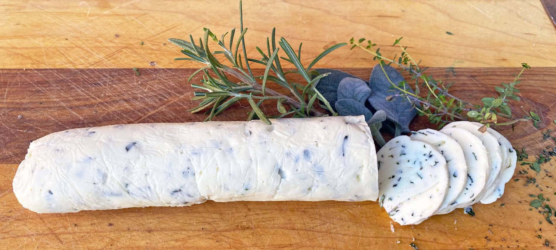 Log of white butter with flecks of herbs in the butter with fresh rosemary, sage leaves, and thyme