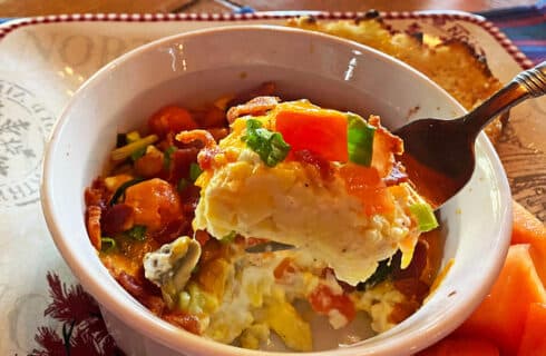 baked eggs in a white dish with tomatoes, onions, bacon and cheese