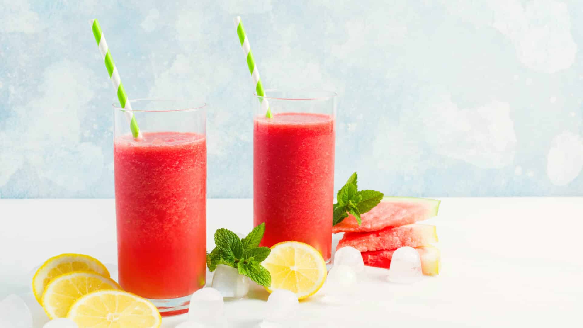 Glasses of red watermelon and lemon slush with lemons, watermelon and lemons, with green and white striped straws