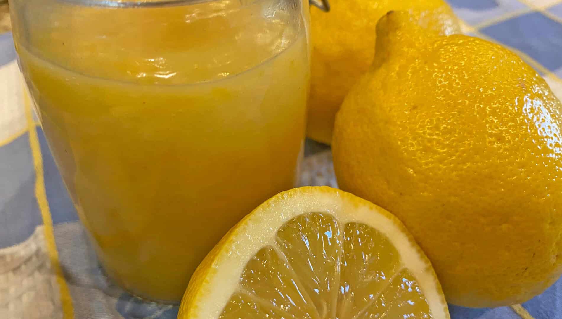 Jar with lemon curd next to whole and cut lemons on a blue and white tea towel