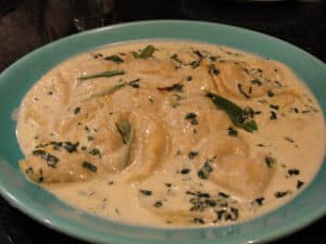 Creamy buttery sauce with bits of green sage leaves and tender ravioli in a blue bowl