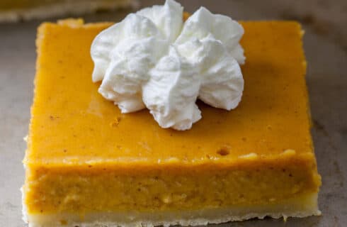 Square orange pumpkin bars with a crust and a dollop of whipped cream