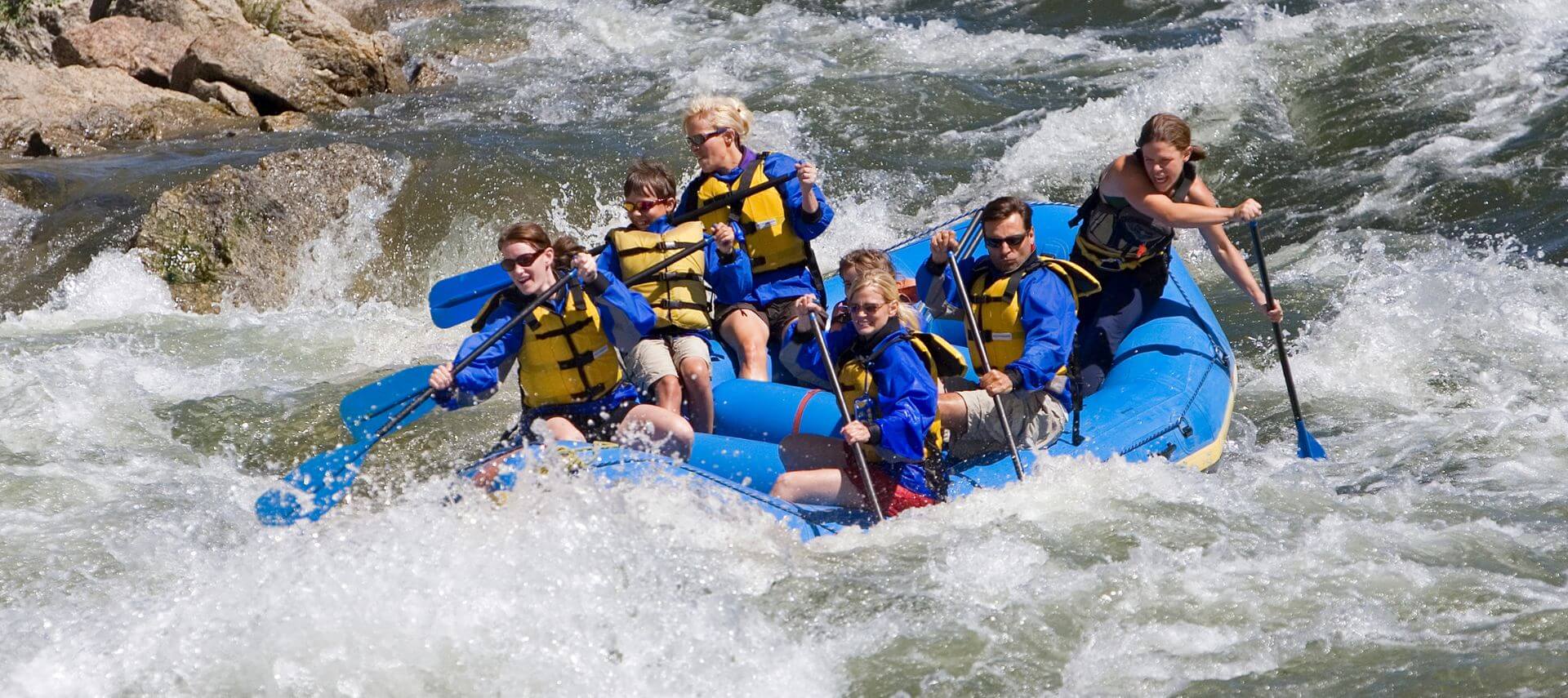 A group of people in blue vests on a blue raft rafting on a wild river.