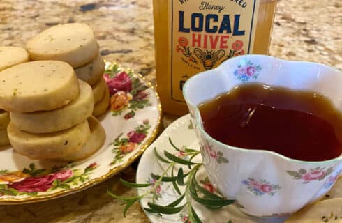 Round shortbread cookies with specs of rosemary along with a cup of tea a a jar of honey