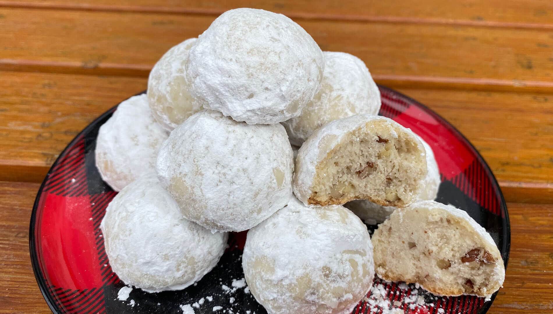 Golden shortbread cookie balls with chopped pecans rolled in white powdered sugar on a black and red checkered plate