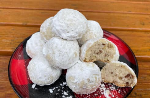Golden shortbread cookie balls with chopped pecans rolled in white powdered sugar on a black and red checkered plate
