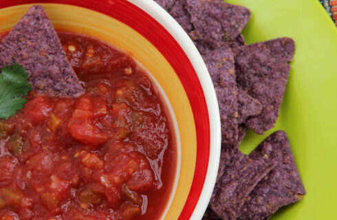 red salsa in a colorful bowl with purple tortilla chips on a green plate