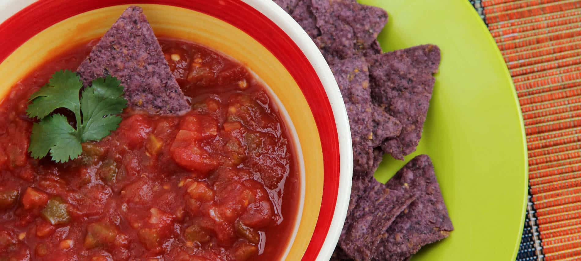 red salsa in a colorful bowl with purple tortilla chips on a green plate