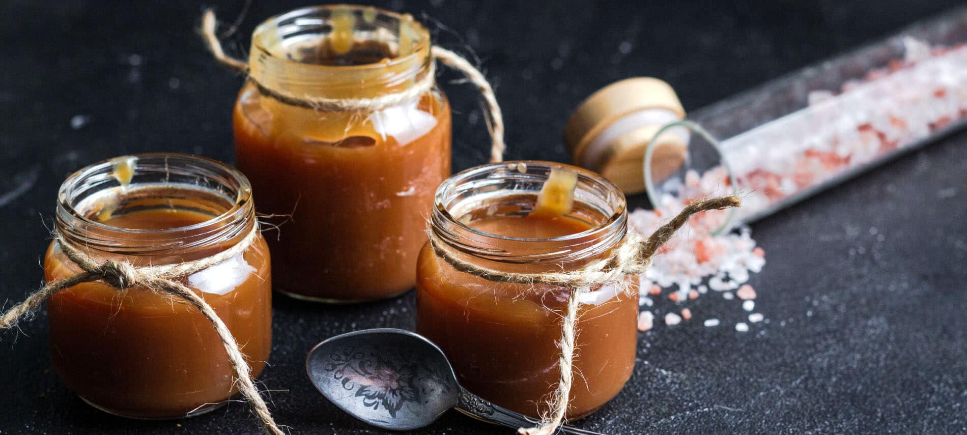 jars of caramel sauce with twine and a spoon, along with chunky sea salt