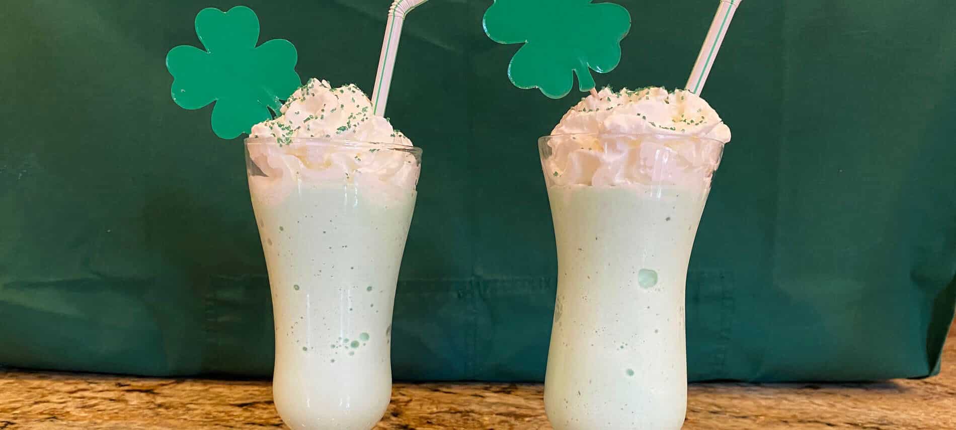 green milkshake with whipped topping and shamrocks in front of a green background