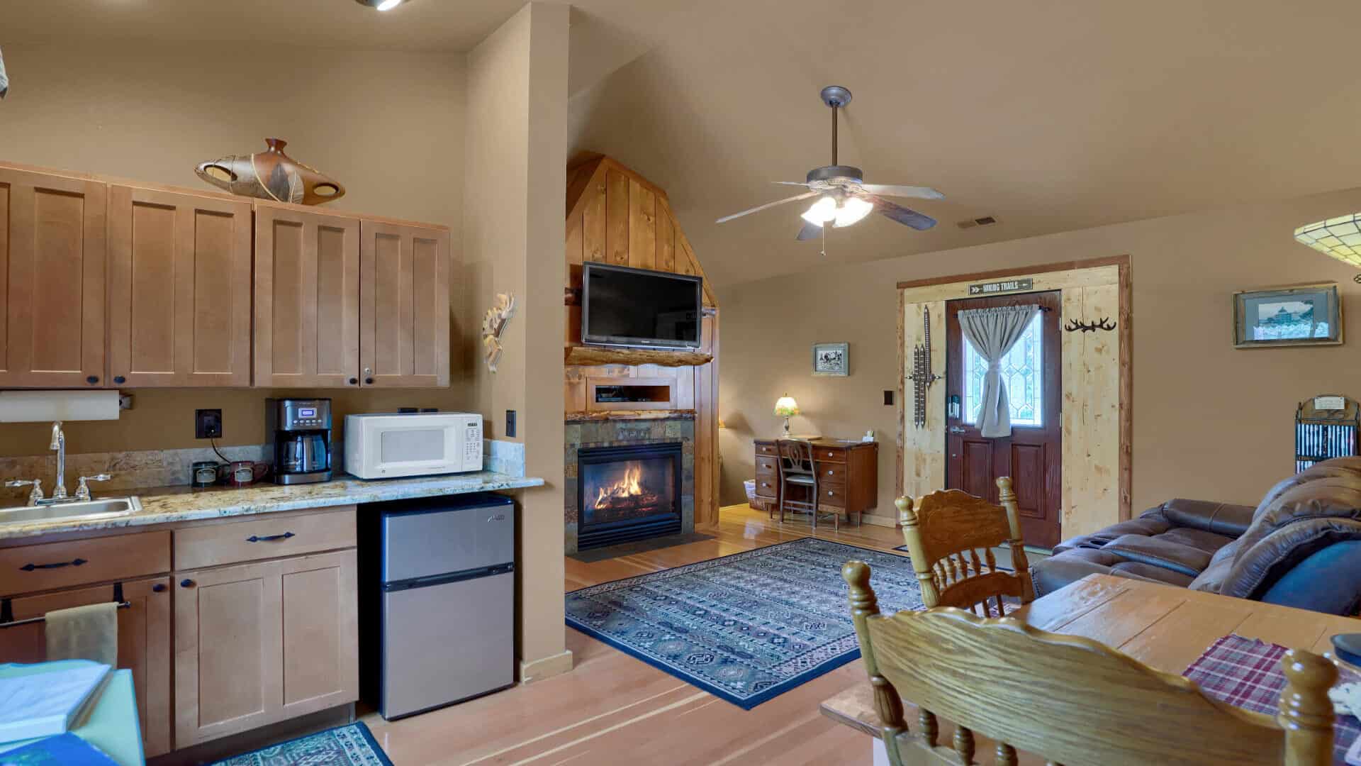 An open floor plan kitchen area, sitting room with fireplace, and writing desk.