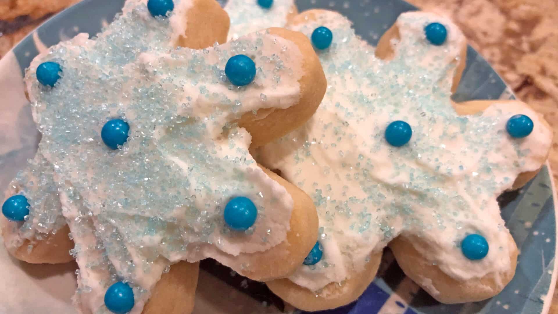 Snowflake shaped thick sugar cookies with white frosting, blue sprinkles, and blue candies