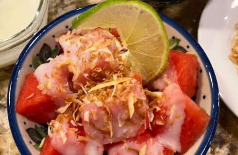 cubes of watermelon with a white coconut cream and golden brown coconut pieces, and a slice of lime