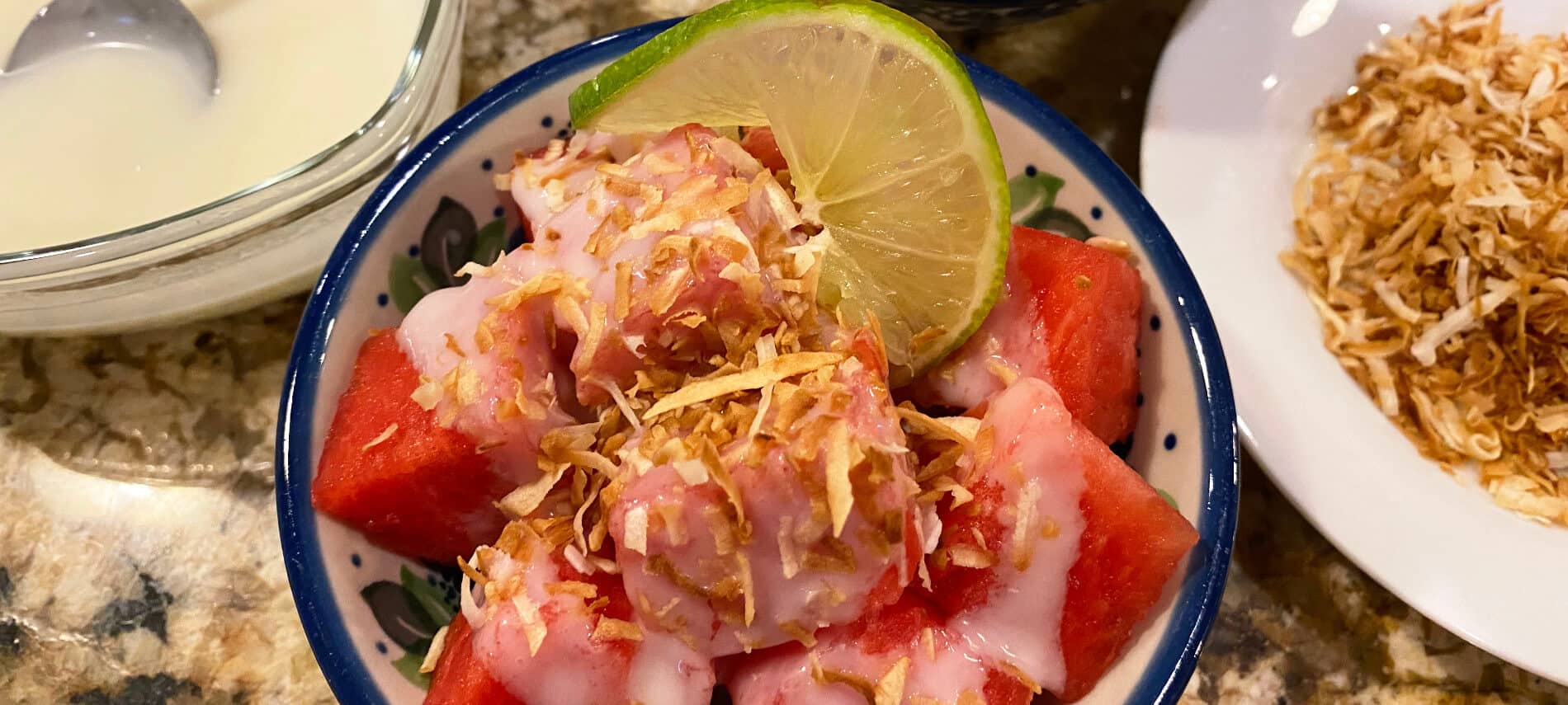 cubes of watermelon with a white coconut cream and golden brown coconut pieces, and a slice of lime