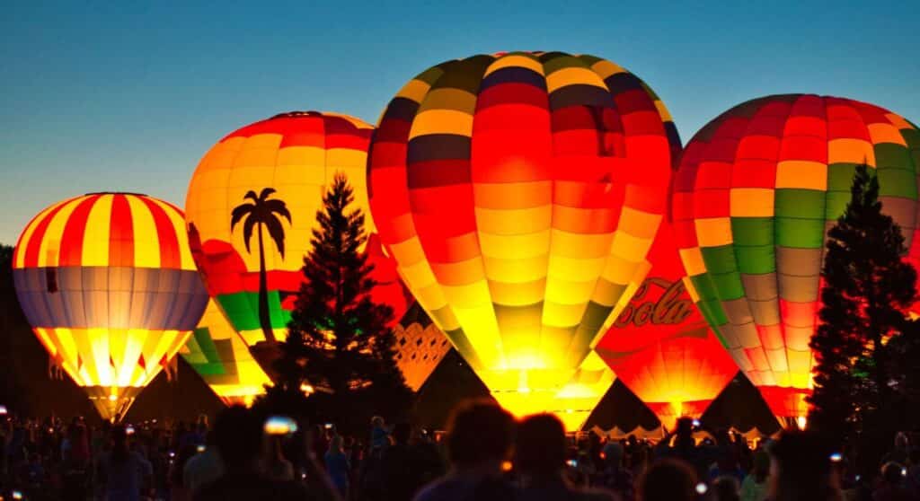 hot air balloons glowing at night with people watching