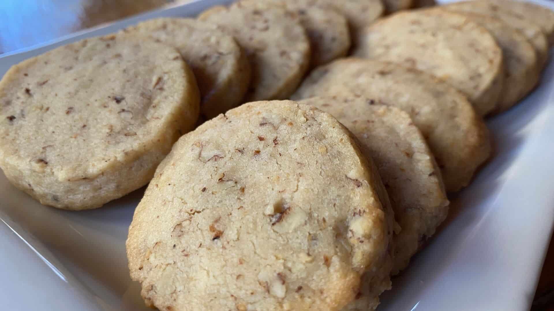 A white tray of thickly sliced round cookies with bits of pecans in them, lightly browned around the edges.
