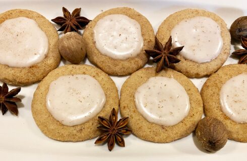 a white plate with several round sugar cookies with dollops of white icing and whole spices around them.