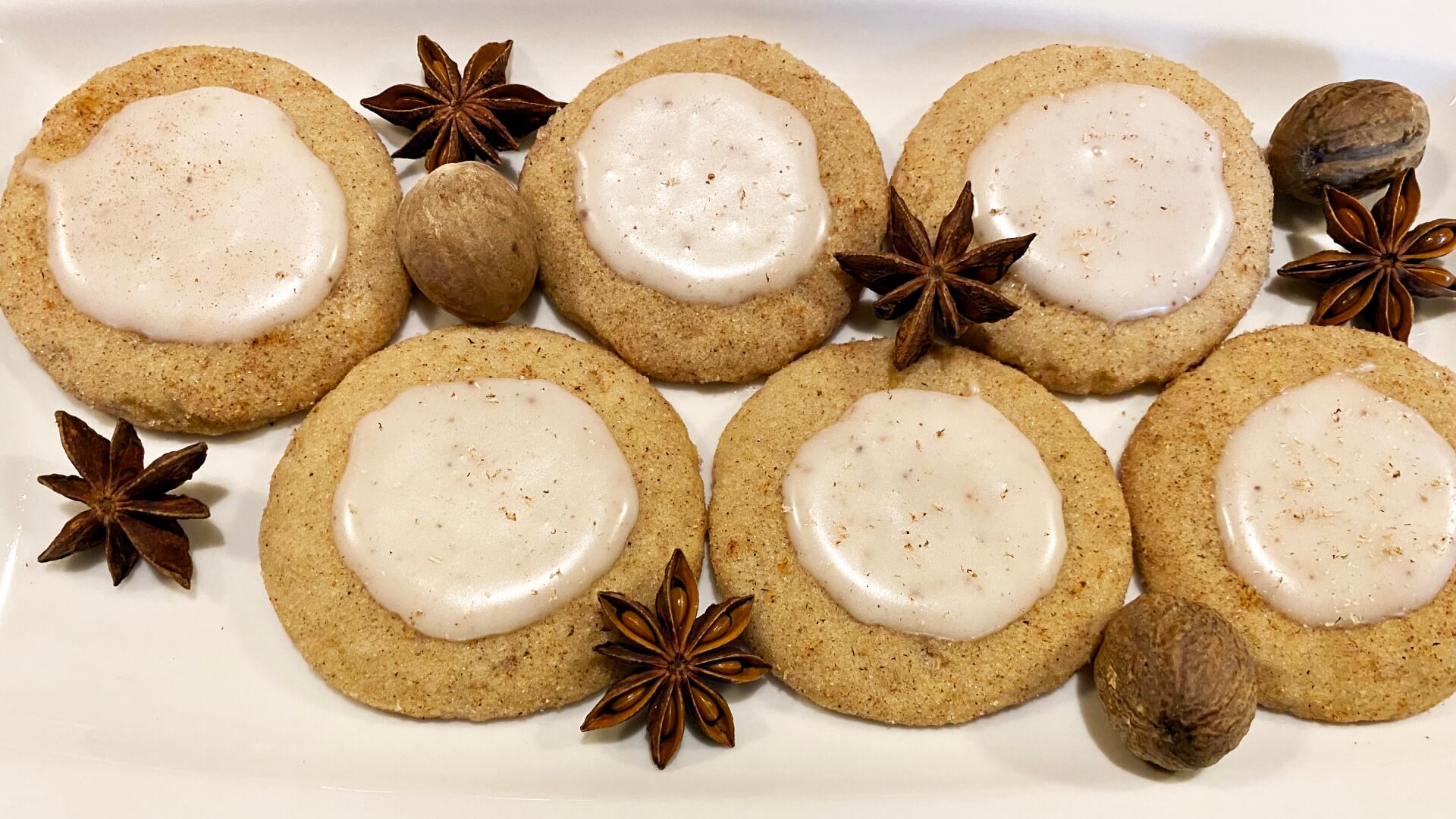 a white plate with several round sugar cookies with dollops of white icing and whole spices around them.