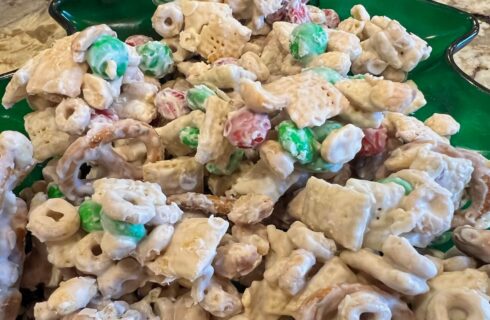 A Christmas candy of Chex® and Cheerios® cereals, peanuts, pretzels, green and red M&Ms®, coated with white chocolate on a green tray.