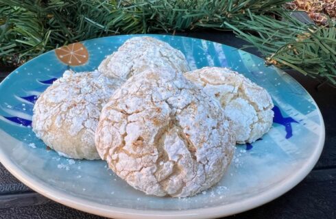 Round cookies baked in powdered sugar with crackles on the top, on a blue plate with pine garland in the background.