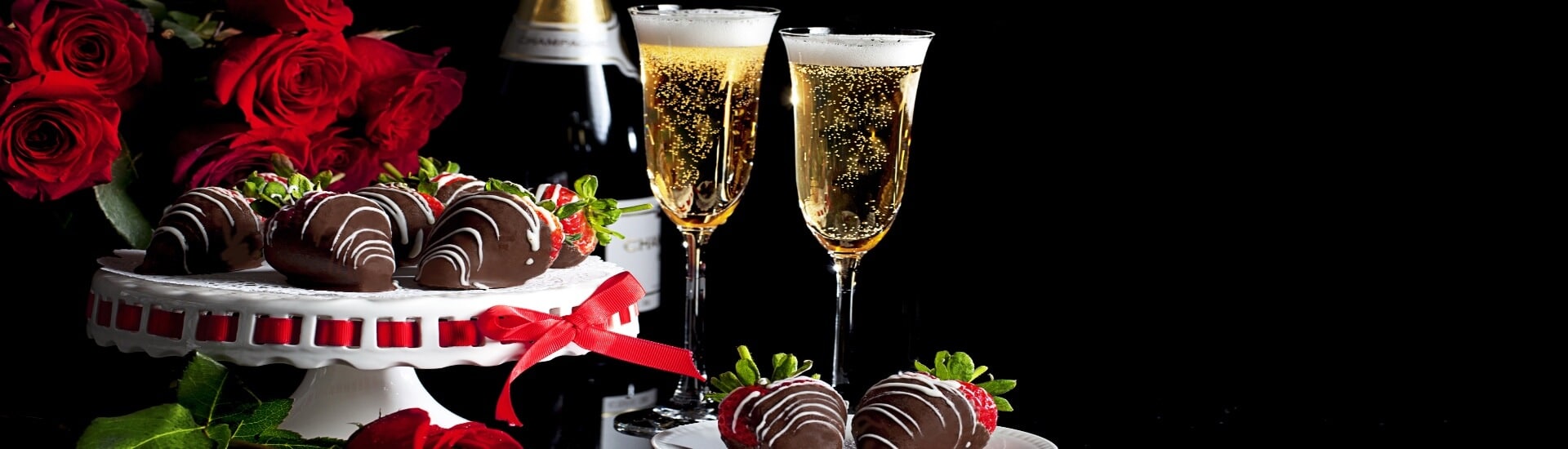a plate of chocolate covered strawberries with a bouquet of roses and 2 glasses of champagne