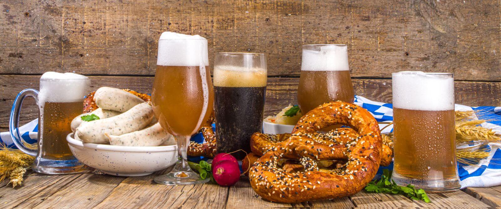 a large soft pretzel and beer with a plate of sausages