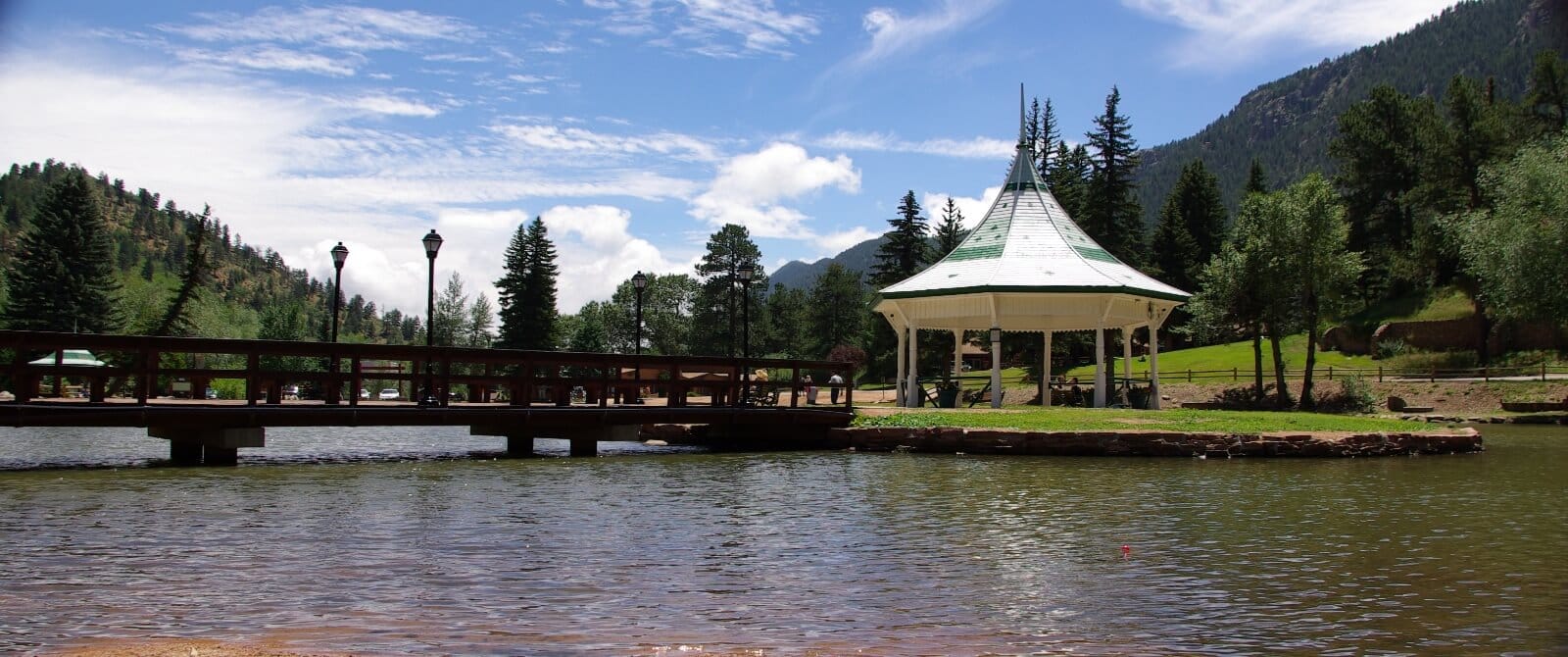 a gazebo on a lake with mountains in the background and blue skies