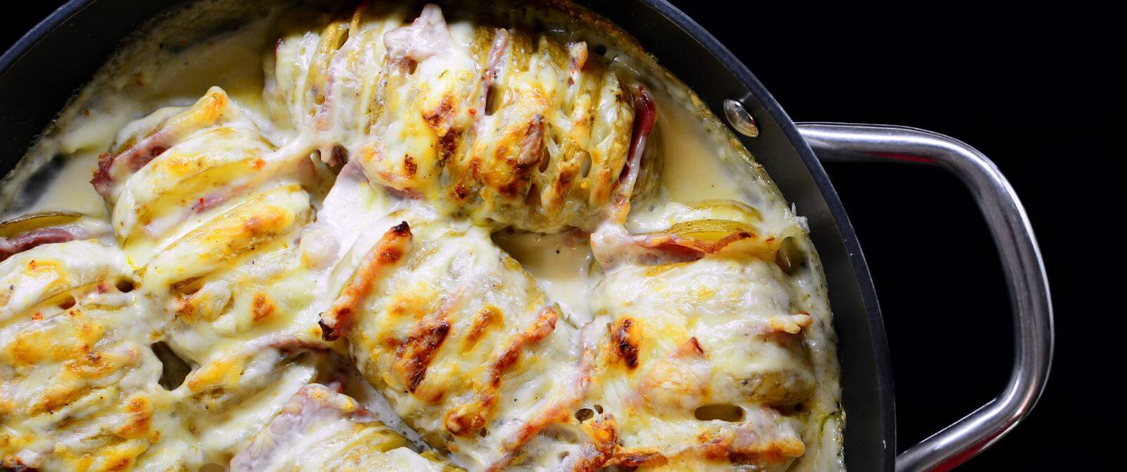a metal pan full of hasselback potatoes covered is broiled cheese