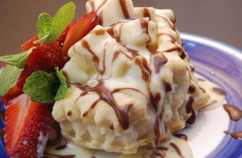 White and blue plate topped with delicious dessert drizzled with brown and white sauce and red strawberries