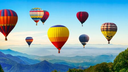 lots of colorful hot air balloons in the air with mountains and trees below them