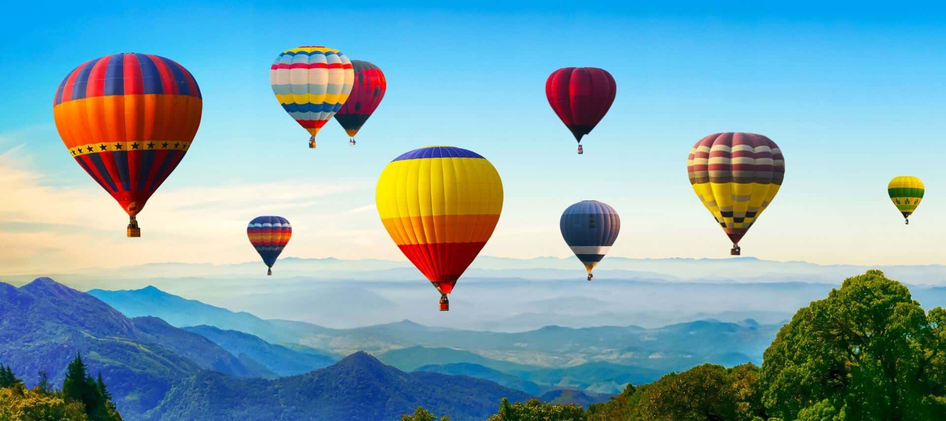 lots of colorful hot air balloons in the air with mountains and trees below them