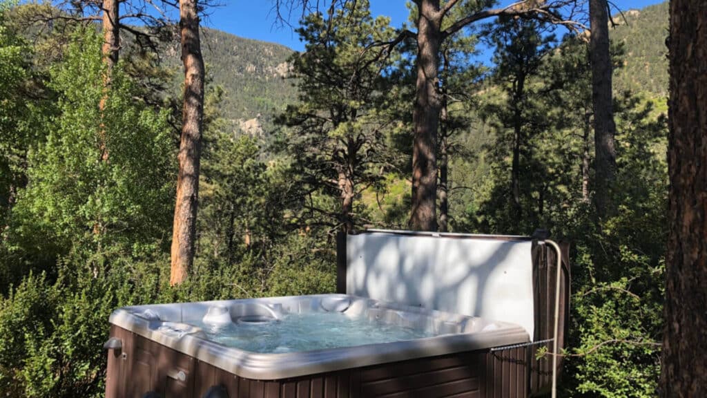 a hot tub with bubbling water in the midst of pine trees and mountains in the background
