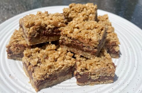 A white speckled plate with square oat cookie bars filled with a chocolate fudgy filling.