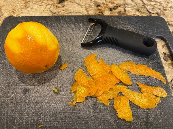 A orange with a potato peeler and grated peels of orange rind.