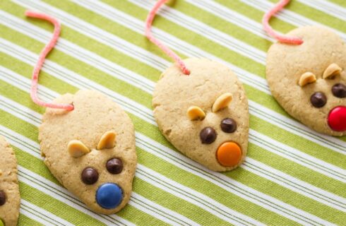 peanut butter cookies shaped like mice with mini chocolate chips and m&m's, peanut ears, and candy tails on a green and white striped cloth