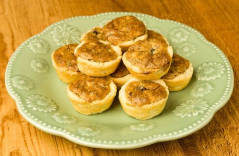 Mini pecan pies on a light green plate on a wood table.